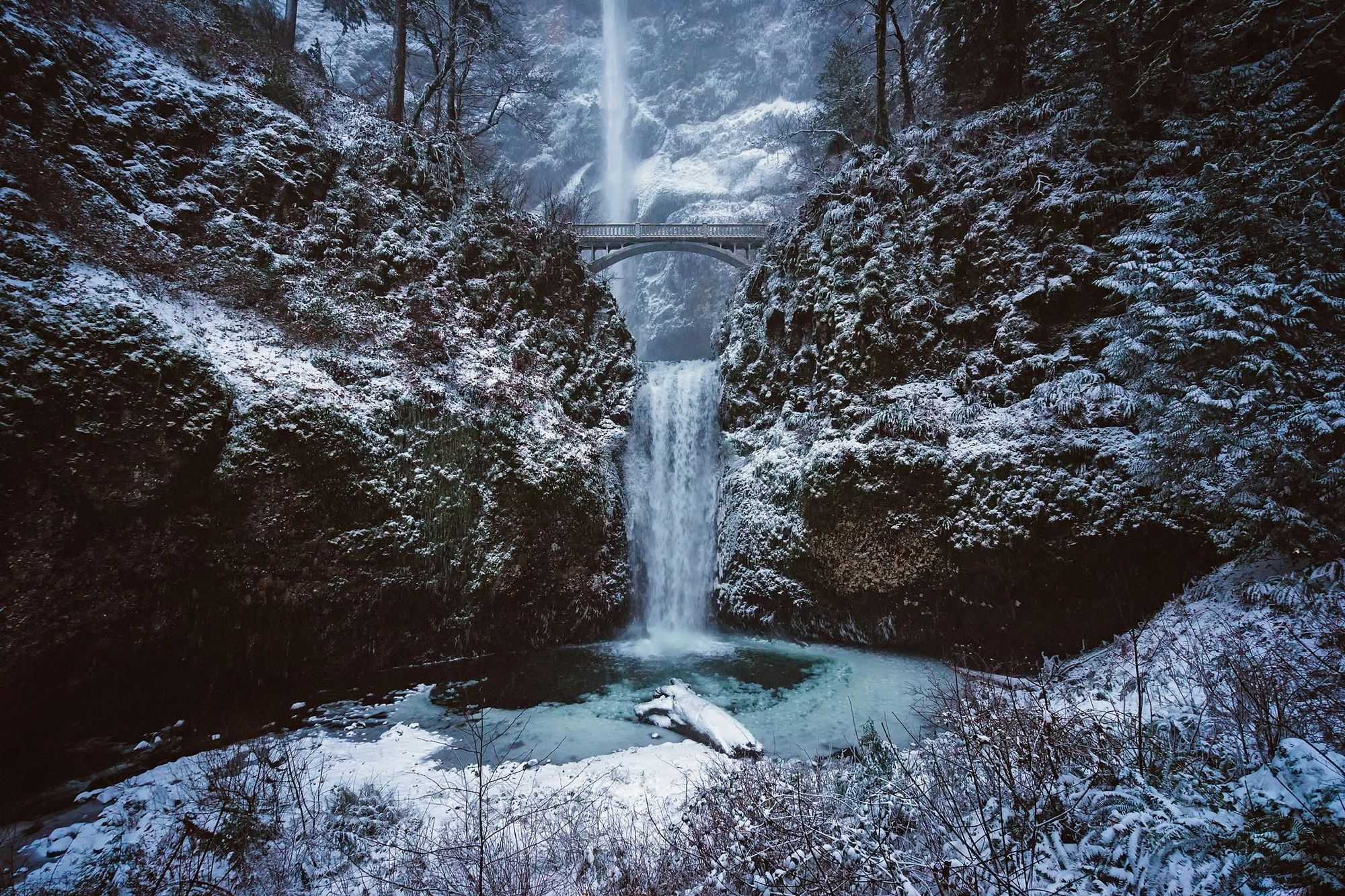 A waterfall falling through a snow covered gorge into a calm pool